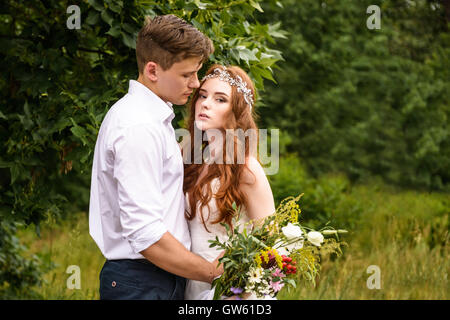 Elegante Braut und Bräutigam zusammen posiert im Freien an einem Hochzeitstag. Braut und Rothaarige Bräutigam in Ähren im Park Stockfoto