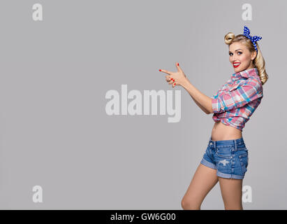 Junge glücklich lächelnde Frau, gekleidet in Pin-Up-Stil etwas zeigen oder Exemplar Bereich für Text oder Slogan. Kaukasische blond-Modus Stockfoto