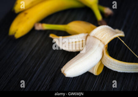 3 reife Bananen, geschält eine Hälfte auf einem dunklen Hintergrund-Nahaufnahme Stockfoto