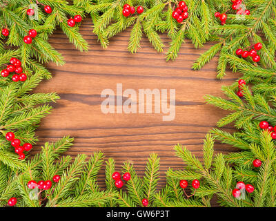 Weihnachtsbaum Äste roten Beeren Rahmen auf strukturierte Holz dunkel Stockfoto