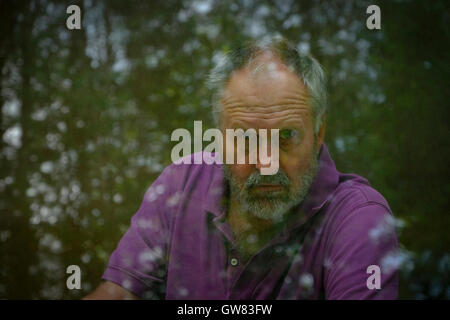 Hübscher bärtigen Mann starrte aus dem Fenster mit Bäumen reflektiert es. Stockfoto
