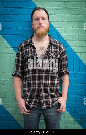 Junge männliche Hipster mit Tätowierung, Flanellhemd, Bart und Baseball cap Stockfoto