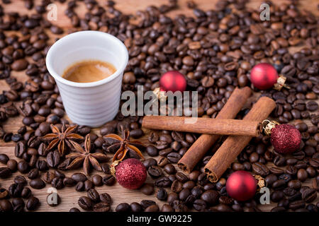 Tasse Kaffee mit Kaffeebohnen, Zimt, Sternanis und rote Weihnachtskugel auf Holz Stockfoto