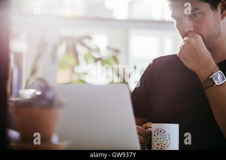 Schwere männliche Führungskraft Blick auf Laptop-Computer. Geschäftsmann sitzt an seinem Schreibtisch mit Tasse Kaffee im Büro. Stockfoto