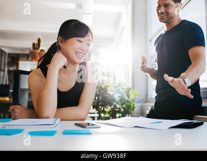 Aufnahme von zwei jungen Geschäftspartnern neue Ideen zu diskutieren und lächelnd. Junge Menschen zusammen arbeiten im Büro. Stockfoto