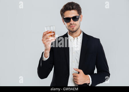 Lächelnd, glücklich Geschäftsmann im Anzug hält Glas Whiskey über grauen Hintergrund Stockfoto