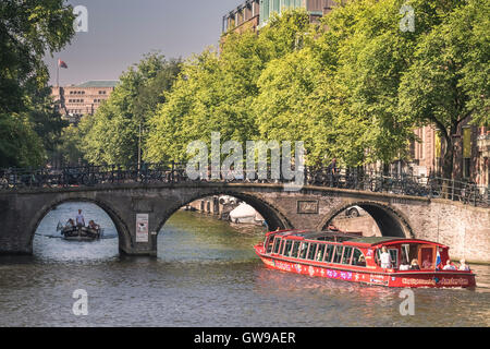 Ausflugsboote gehen unter Amstel-Brücke, an der Kreuzung des Flusses Amstel und Herengracht Kanal, Amsterdam, Niederlande. Stockfoto