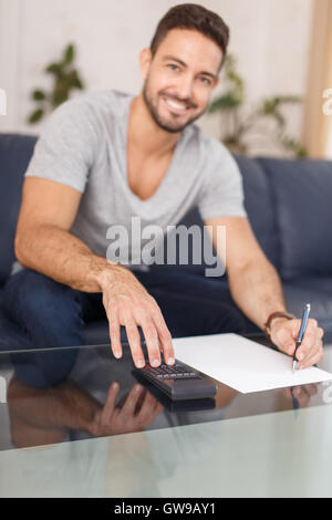 Glücklicher Mann Berechnung indoor, schreiben auf weißes Papier mit Bleistift, mit Taschenrechner. Stockfoto