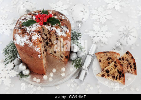 Italienische Schokolade Panettone Weihnachtskuchen und Scheibe mit Beeren der Stechpalme, Silber und weiß Tand und Schneeflocke Dekorationen. Stockfoto