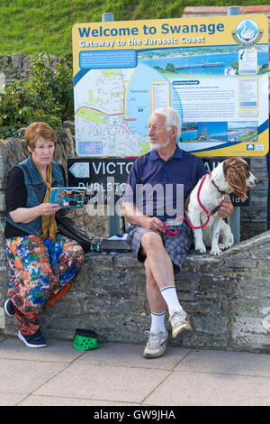 Paar sitzt an Wand mit Hund willkommen, Swanage Zeichen betrachten Swanage Folk Festival-Programm im September Stockfoto