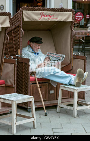 Senioren, die Zeitung zu lesen, während im Strandkorb in einem Café an der Ostseeküste in Deutschland sitzen Stockfoto