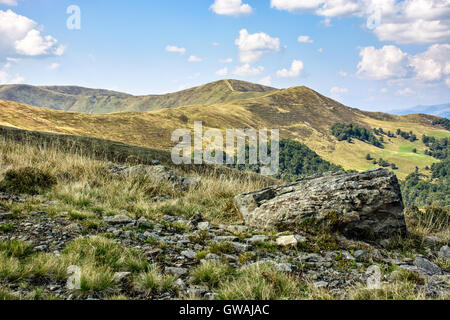 Landschaft mit Steinen unter dem Rasen am Hang vor Bergspitze unter blauem Himmel mit Wolken Stockfoto