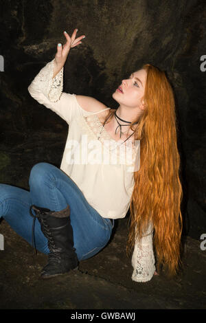 Schöne rote Kopf in skinny-Jeans, weißes Top und schwarze Stiefel, gefährlich sitzt in der Ecke einer kleinen Höhle auf einen alten Tunnel. Stockfoto