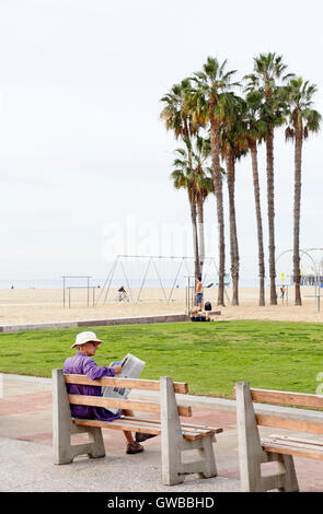 Santa Monica, Los Angeles, Kalifornien. Mann News lesen Papier auf einer Bank am Strand. Stockfoto