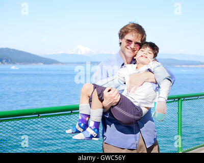 Vater holding deaktiviert Sohn in Armen an Deck der Fähre. Stockfoto