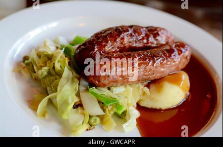 Würstchen und Kartoffelbrei mit saisonalen Gruenen mit Rotwein Soße auf einem weißen Teller serviert - Filter angewendet Stockfoto