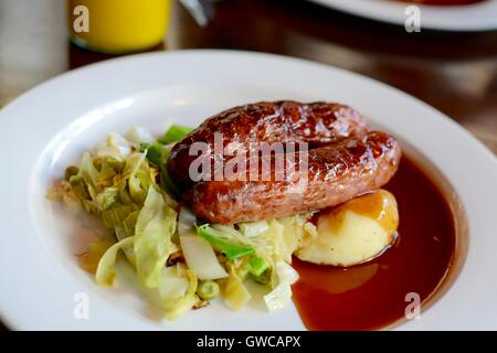 Würstchen und Kartoffelbrei mit saisonalen Gruenen mit Rotwein Soße auf einem weißen Teller serviert - Filter angewendet Stockfoto