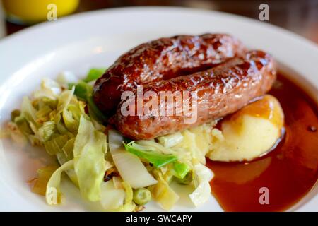 Würstchen und Kartoffelbrei mit saisonalen Gruenen mit Rotwein Soße auf einem weißen Teller serviert - Filter angewendet Stockfoto