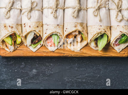 Tortilla wraps mit verschiedenen Füllungen auf Holzbrett über konkrete Hintergrund dunkel grau Grunge, Draufsicht, Textfreiraum, horizontale Stockfoto