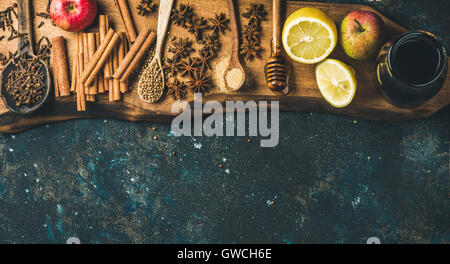 Zutaten für die Herstellung von Glühwein. Wein in Glasflasche, Honig, Zitrone, Äpfel und Gewürzen auf Holzbrett über alte blau lackiert Stockfoto