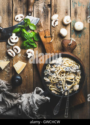 Abendessen im italienischen Stil. Cremige Champignon Nudeln Spaghetti in gusseisernen Pfanne auf Holzbrettern mit Parmesan-Käse, Blätter frisches Basilikum Stockfoto