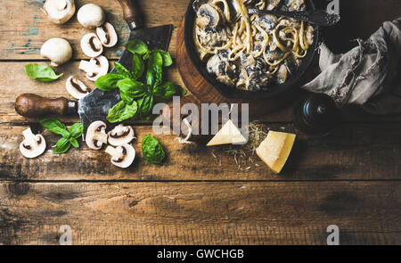 Abendessen im italienischen Stil. Cremige Champignon Nudeln Spaghetti in Gusseisen Pfanne mit Parmesan-Käse, frischem Basilikum und Pfeffer über alte rus Stockfoto