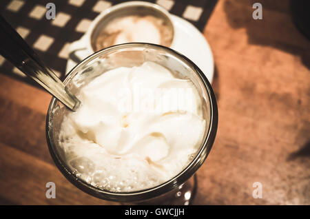 Tasse Kaffee mit Schlagsahne steht auf Holztisch in der Cafeteria. Nahaufnahme Foto mit selektiver Weichzeichner Stockfoto