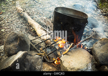 Alte gebrauchte schwarze Pfanne mit kochendem Wasser steht auf einem Lagerfeuer Stockfoto