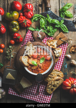 Hausgemachte italienische geröstete Tomaten und Knoblauch Suppe in Schüssel auf Runde servieren Board mit Basilikum, Parmesan-Käse und Brot über alte ru Stockfoto