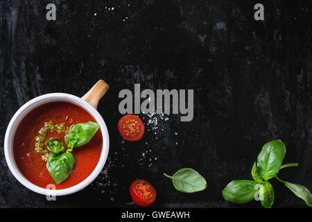 Keramische Tasse Tomatensuppe Gazpacho mit grünem Pesto-Sauce, Salz und Basilikum über altes schwarzes Eisen-Hintergrund mit Textfreiraum. Top v Stockfoto
