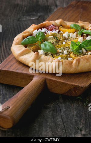 Hausgemachte offen Gemüsetorte Galette mit bunten Tomaten, Tomatenpesto, Feta-Käse und frischem Basilikum, serviert auf Holz hacken b Stockfoto