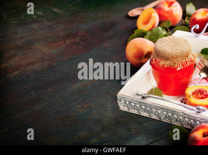 Pfirsichmarmelade mit frischen Pfirsichen auf rustikalen Tisch. Stockfoto