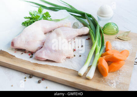 Rohe Hähnchenschenkel mit Gemüse und Gewürzen auf ein Schneidebrett aus Holz angeordnet. Weiße Holz rustikal Hintergrund. Stockfoto