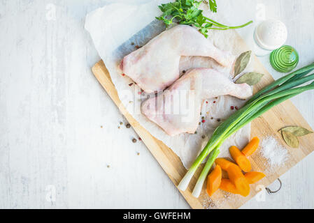 Rohe Hähnchenschenkel mit Gemüse und Gewürzen auf ein Schneidebrett aus Holz angeordnet. Weiße Holz rustikal Hintergrund. Stockfoto