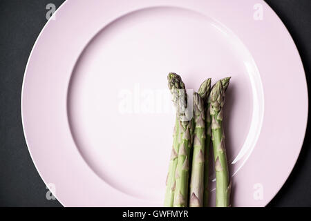 Grüner Spargel auf einen rosa Teller und schwarze Tischplatte Bund grüner Spargel Stockfoto