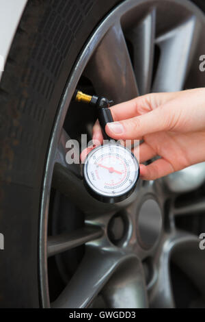 Nahaufnahme von Frau Auto Reifendruck mit Manometer überprüfen Stockfoto