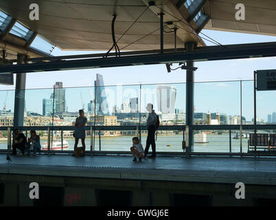 Menschen warten auf die Plattform in London Blackfriars Station, die auf einer Schiene positioniert ist Brücke über die Themse. Stockfoto