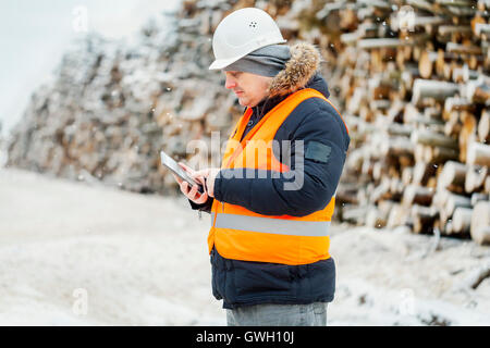 Ingenieur mit Tablet PC in der Nähe von Haufen von Protokollen im winter Stockfoto