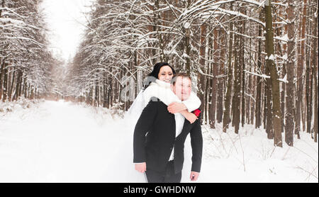 Mann und Frau Huckepack Fahrt auf Winterurlaub im verschneiten Wald. Stockfoto