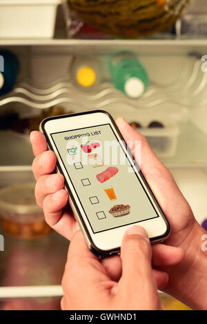 junger Mann, der seine Einkaufsliste in seinem Smartphone, mit Bildern von verschiedenen Produkten, fotografiert von mir in seinem Bildschirm, vor Stockfoto