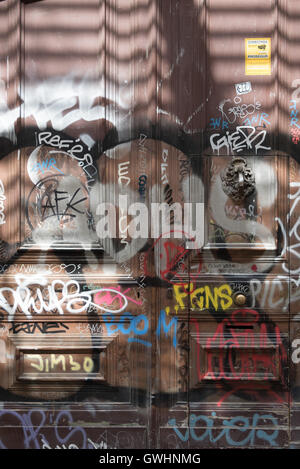 Hell Graffiti bedeckt Tür teilweise Sonne Teil Schatten entlang einen Durchgang nach unten Carrer del Cardenal Casanas, Barcelona, Spanien. Stockfoto