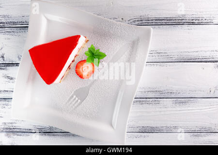 Stück Gelee-Torte mit Erdbeeren auf weißem Hintergrund aus Holz. Stockfoto