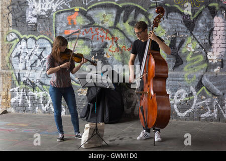 Ein paar Musiker als Straßenmusikant unter einer Eisenbahnbrücke auf Clink Street, London Stockfoto