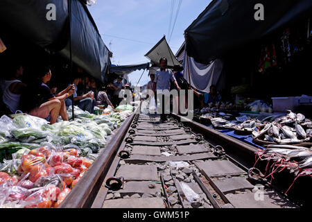 Händler, die Lebensmittel auf dem Maeklong Railway Market verkaufen, auch bekannt als „Schirm Pulldown Market“ oder Talat Rom Hup., der sich auf einer Reihe von Eisenbahngleisen befindet, die direkt durch das Marktgebiet führen, wo die Händler ihre Verkaufsstände und einziehbaren Markisen schnell anpassen, um den Zug passieren zu lassen, und dann schnell wieder Geschäfte aufnehmen, als wäre nichts passiert. Das Hotel befindet sich in Samut Songkhram, etwa 37 Meilen westlich von Bangkok, Thailand Stockfoto
