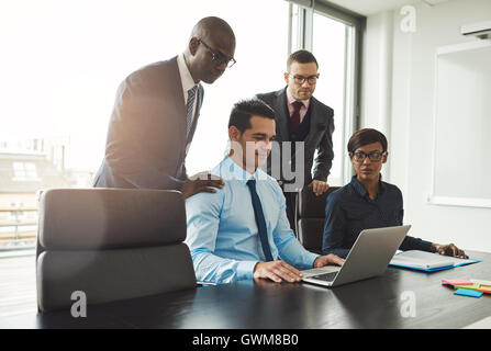 Freundliche Gruppe von vielfältigen junge Geschäftsleute in der formalen Kleidung Blick auf Laptop am Konferenztisch vor großen windo Stockfoto