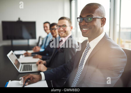Lächelnde zuversichtlich afrikanischen Geschäftsmann in einem Gespräch mit einer Gruppe von Rassen Mitarbeiter sitzen an einem Konferenztisch in der von Stockfoto