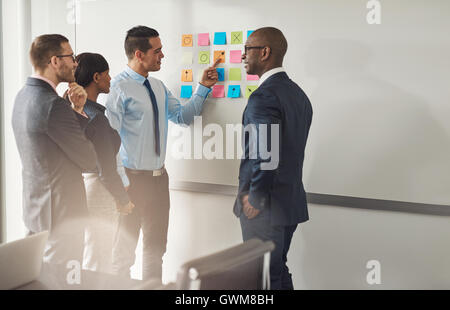 Gruppe von Rassen Geschäftsleute stehen im Chat, wie sie auf eine Reihe von bunten Memos an der Wand, ein Profi zu lösen versuchen zeigen Stockfoto