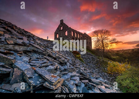 Eine einsame Gestalt steht bei Ynys y Pandy stillgelegten Schiefer Mühle bei Sonnenuntergang, Cwmystradllyn, Snowdonia National Park, North Wales, UK Stockfoto