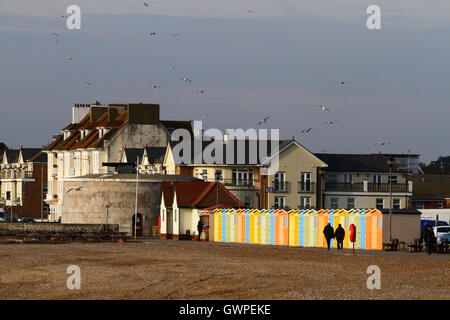 Menschen zu Fuß vorbei an Linie der hölzernen Umkleidekabinen am Meer auf eine Winter-Nachmittag, Seaford, East Sussex, England Stockfoto