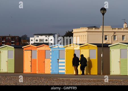 Älteres Ehepaar vorbeigehen Linie der hölzernen Umkleidekabinen am Meer auf einer Winter-Nachmittag, Seaford, East Sussex, England Stockfoto